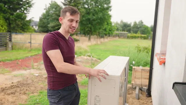 Dawid Jarząbek przy jednostce zewnętrznej pompy ciepła obok nowego domu parterowego