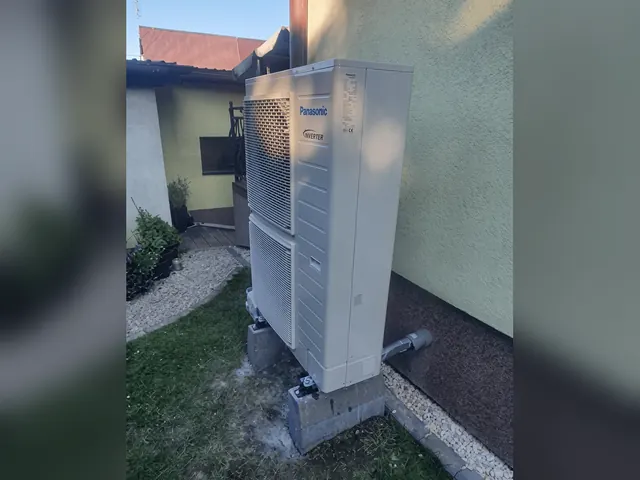 Jednostka zewnętrzna pompy ciepła Panasonic 12 kW przy kremowej ścianie domu w Jastrzębiu-Zdroju, obok trawnik