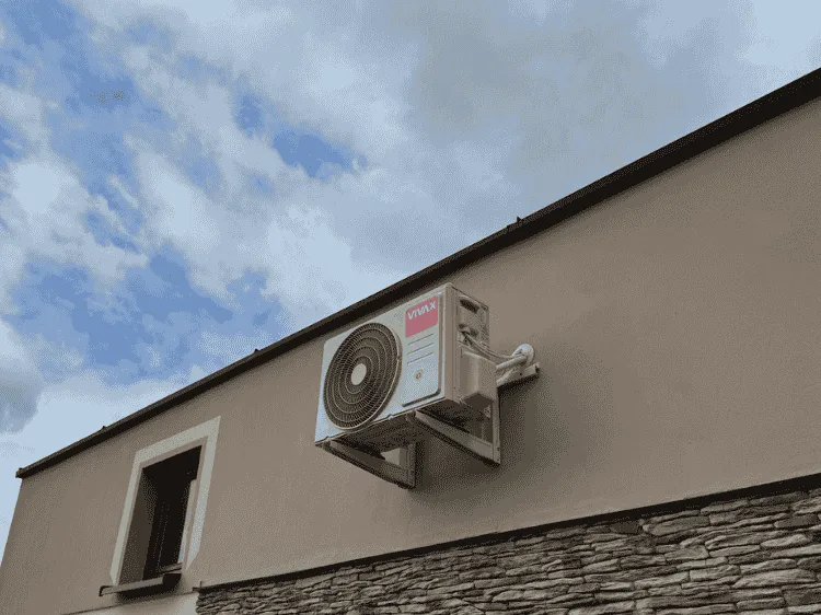 Jednostka zewnętrzna klimatyzatora wysoko na elewacji z okładziną kamienną
