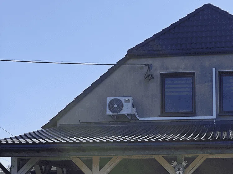 Jednostka zewnętrzna klimatyzatora na szczycie domu z ciemnym dachem