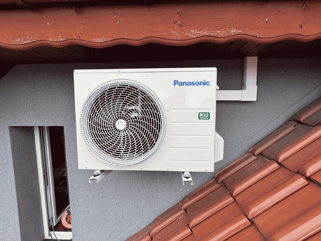 Klimatyzacja, Rydułtowy: Jednostka zewnętrzna klimatyzatora Panasonic na szarej ścianie obok czerwonej dachówki