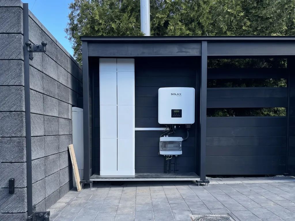 Magazyn energii, Żory: Zewnętrzna czarna zabudowa z białą wieżą magazynu energii i falownikiem Solax przy płocie z bloczków