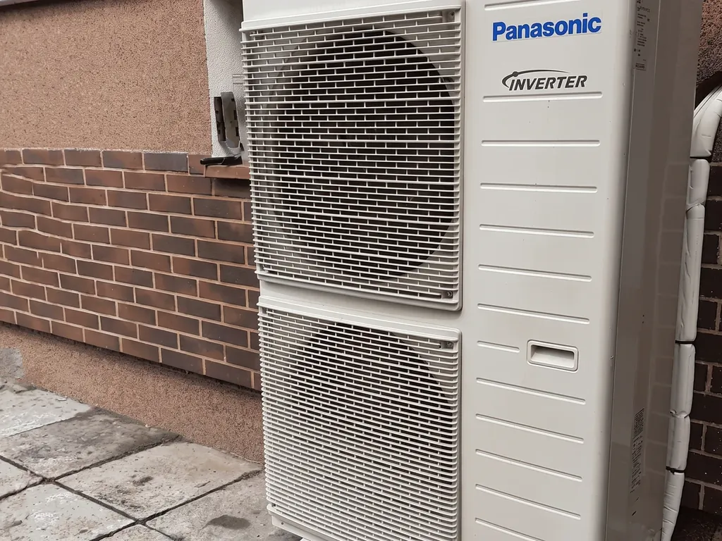 Pompa ciepła, Golasowice: Jednostka zewnętrzna Panasonic Inverter (dwa wentylatory) przy ścianie z płytkami ceglanymi, kostka
