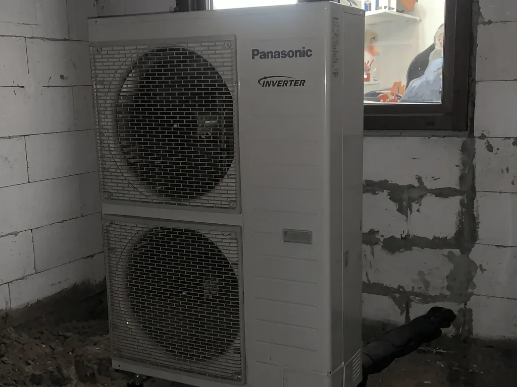 Pompa ciepła, Racibórz: Jednostka zewnętrzna Panasonic przy ścianie z bloczków i oknie (nowa budowa)