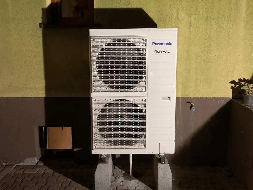 Pompa ciepła, Olza: Jednostka zewnętrzna Panasonic na tarasie przy żółtej ścianie, wieczorem z lampą błyskową